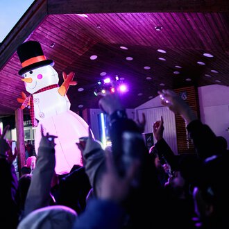 A festive event with a large snowman puppet and many celebrating people. Colorful lights illuminate the scene. | © Kleinwalsertal Tourismus | Oliver Farys