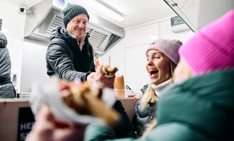 A vendor serves ice cream to happy customers in a food truck. The two women are laughing and enjoying the delicious treats. | © Kleinwalsertal Tourismus | Oliver Farys