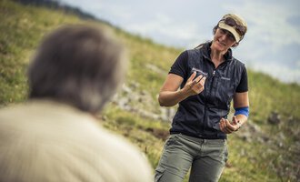 A woman is talking to a man outdoors. She is holding an object in her hand and smiling kindly. | © Kleinwalsertal Tourismus | Oliver Farys