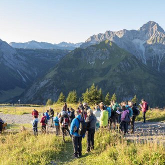 A group of hikers enjoys the view of the mountains. The sky is clear, and nature provides an impressive backdrop. | © OK-Bergbahnen