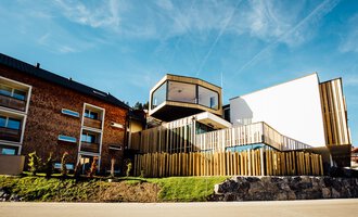 Ein modernes Gebäude mit Holzverkleidung und großen Fenstern. Die Architektur kombiniert traditionelle und zeitgenössische Elemente. | © Genuss- und Aktivhotel Sonnenburg | Andi Mayr