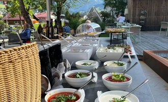 Ein schön gedeckter Tisch im Freien mit verschiedenen Schüsseln voller frischer Salate und Suppen. Im Hintergrund sind Bäume und eine einladende Terrasse zu sehen. | © Genuss- und Aktivhotel Sonnenburg