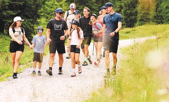 Two hikers walk along a path in the mountains. The sun is shining and the landscape is green and golden. | © Kleinwalsertal Tourismus eGen - Fotograf: Oliver Farys