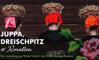 An exhibition about Walser attire featuring three individuals wearing traditional clothing and intricately designed headgear. The background is wood-colored and the colors of the clothing are striking.