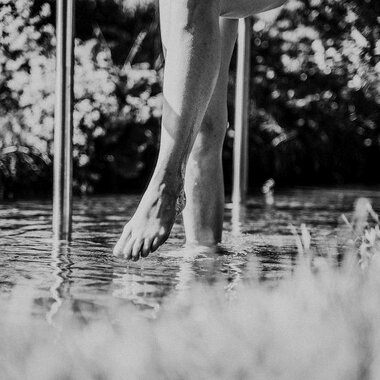 Ein Fuß steht im Wasser, umgeben von grünem Gras. Die Aufnahme ist in Schwarz-Weiß gehalten und vermittelt eine ruhige Atmosphäre. | © Das Naturhotel Chesa Valisa****s