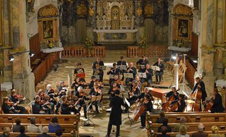 Ein Orchester spielt in einer Kirche, umgeben von kunstvollen Verzierungen. Das Publikum sitzt in den Bänken und lauscht der Musik. | © Collegium Instrumentale Stuttgart