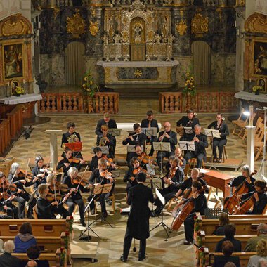 Ein Orchester spielt in einer Kirche, umgeben von kunstvollen Verzierungen. Das Publikum sitzt in den Bänken und lauscht der Musik. | © Collegium Instrumentale Stuttgart
