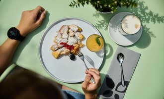 A plate with sweet pastries, powdered sugar, and berries, along with a glass of juice and a cup of coffee. The scene is on a green table. | © Kleinwalsertal Tourismus | Oliver Farys