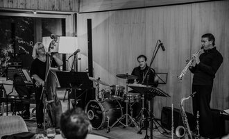 Three musicians are happily gathered together, playing various instruments. In the background, the nature hotel can be seen. | © Naturhotel Chesa Valisa