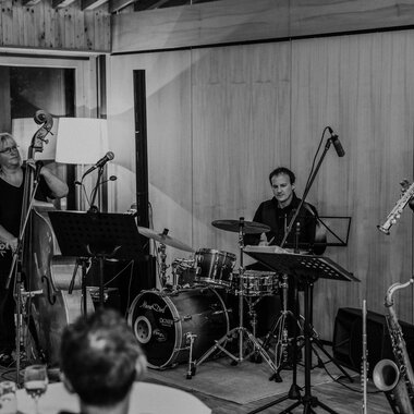 Three musicians are happily gathered together, playing various instruments. In the background, the nature hotel can be seen. | © Naturhotel Chesa Valisa