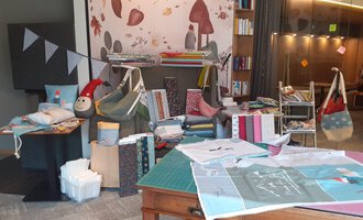 A cozy room with various fabrics, bags, and decorations. On the wall, colorful patterns and a small doll can be seen. | © Der Kleinwalsertaler Rosenhof | Dominik Berchtold