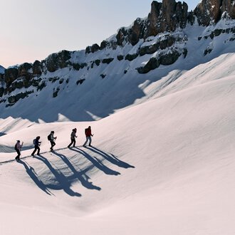 A group of hikers is walking through a snowy landscape. Majestic mountains can be seen in the background. | © Kleinwalsertal Tourismus eGen | Oliver Farys