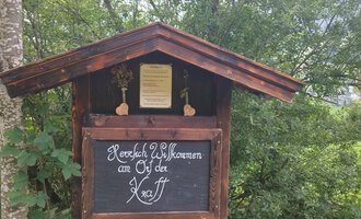 A heartfelt welcome sign at a wooden building in nature. Surrounded by trees and green landscape. | © Nicole Lughammer