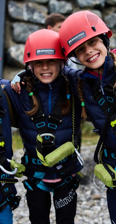 Three cheerful children in climbing helmets and safety harnesses are smiling at the camera. They are ready for an exciting adventure in nature. | © Kleinwalsertal Tourismus | Oliver Farys