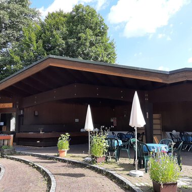 Ein gemütliches Café mit einer Holzfassade und Terrassenmöbeln. Umgeben von Pflanzen und Bäumen, lädt es zum Entspannen ein. | © Kulturcafe Kleinwalsertal | Veronika Senn