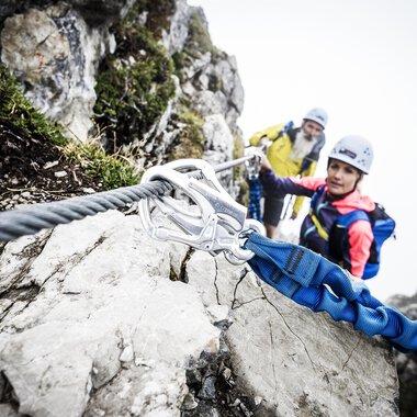 Two climbers are securing themselves on a steep rock. It is foggy, and the surroundings seem challenging and adventurous. | © Bergschule Kleinwalsertal | Dominik Berchtold