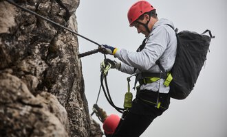 A climber is secured to a rock wall and is focusing on his technique. In the background, another climber can be seen, while a misty atmosphere prevails. | © Bergschule Kleinwalsertal | Oliver Farys