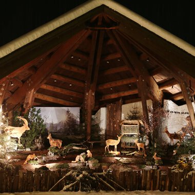 A festive setting with a wooden structure and illuminated animals. In the background, Christmas trees and a winter landscape can be seen. | © Kleinwalsertal Tourismus | Frank Drechsel