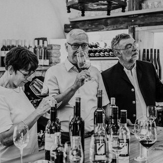 © Das Naturhotel Chesa Valisa A group of three people is enjoying wine in a wine shop. They are holding glasses in their hands and are looking intently at the glasses. | © Das Naturhotel Chesa Valisa