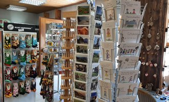 A cozy shop with a display stand for postcards and souvenirs. In the background, colorful socks and other gift items can be seen. | © Abler Mitbringsel Riezlern | Veronika Senn