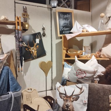 Ein gemütlicher Raum mit verschiedenen Kissen und Dekorationsartikeln. Auf einem Regal befinden sich Artikel mit Tiermotiven und Holzaccessoires. | © Abler Mittelberg | N. Lughammer