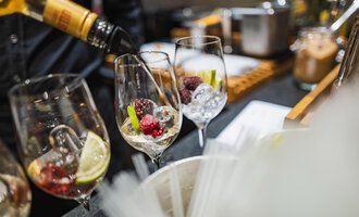 Gläser mit frischen Beeren und Eis werden gefüllt. Im Hintergrund sind Cocktail-Zutaten sichtbar. | © Verwöhn- und Wellnesshotel Walserhof | Frank Simon