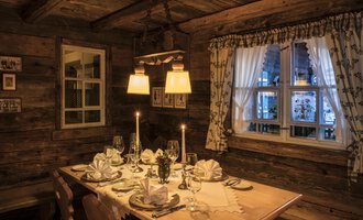 A cozy restaurant with a beautifully set table. The warm lights and wooden walls create an inviting atmosphere. | © Alpahotel Walserstuba GmbH Patrik Säly Photography
