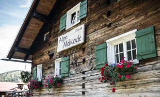 A traditional wooden house with green shutters. Flower boxes with colorful flowers adorn the windows. | © Kleinwalsertal Tourismus | Andre Tappe