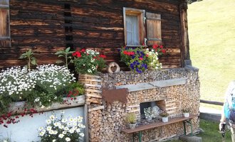 A traditional wooden house with colorful flowers and wood piles. The place radiates rural coziness and a connection to nature. | © Kleinwalsertal Tourismus | N. Lughammer