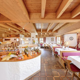 An inviting restaurant with a wooden ceiling and tables set for guests. In the background, a selection of jams and foods is visible on a buffet. | © Alpengasthof Hörnlepass | Monschau Michael