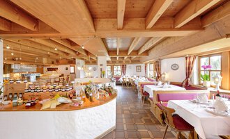 An inviting restaurant with a wooden ceiling and tables set for guests. In the background, a selection of jams and foods is visible on a buffet. | © Alpengasthof Hörnlepass | Monschau Michael