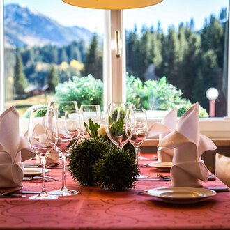 A beautifully set table with glasses and folded napkins. In the background, there is a view of mountains and trees. | © Alpenhotel DAS KÜREN