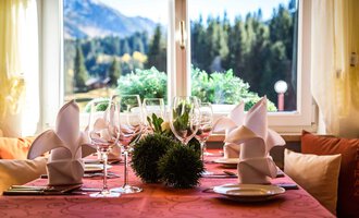 A beautifully set table with glasses and folded napkins. In the background, there is a view of mountains and trees. | © Alpenhotel DAS KÜREN