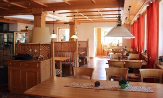 A cozy restaurant with wooden interiors and large windows. Red curtains and well-set tables create an inviting atmosphere.