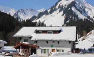 A picturesque hotel in the Alps, surrounded by snow-covered mountains. The landscape is wintry and inviting.