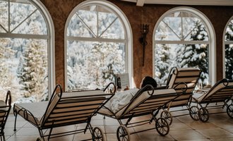 A cozy room with loungers and large windows. Outside, there is a winter landscape with snow and trees visible. | © Verwöhn- & Wellnesshotel Walserhof| Aileen Melucci