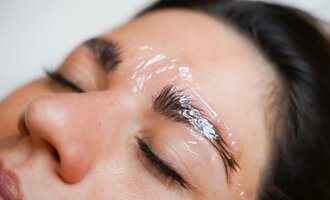 A person is receiving a cosmetic treatment with a transparent gel mask on their eyebrows. They are lying back relaxed with their eyes closed. | © Annett Schwärzler Nails & Spa | Stefanie Haid