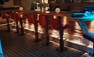 Eine gemütliche Bar mit roten Hochstühlen und einer Holztheke. Der Raum ist sanft beleuchtet und sorgt für eine entspannte Atmosphäre. | © Hotel Steinbock