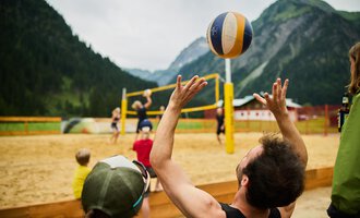 A sand volleyball game in the mountains. Players throw the ball into the air while others watch. | © Kleinwalsertal Tourismus | Oliver Farys