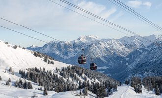 A winter landscape with snow-covered mountains and ski lifts. In the background, there's a clear sky and beautiful fir trees. | © OBERSTDORF · KLEINWALSERTAL BERGBAHNEN
