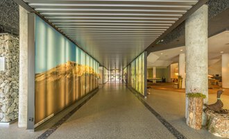 A modern entrance area with bright walls and a long hallway. On both sides, creative wall designs can be seen. | © Kleinwalsertal Tourismus |  Steffen Berschin