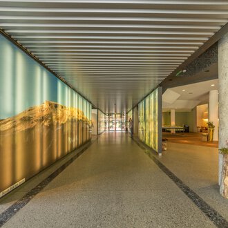 A modern hallway with large wall pictures and an open reception area. The walls are designed with soft colors and beautiful landscapes. | © Kleinwalsertal Tourismus |  Steffen Berschin
