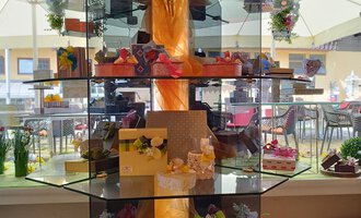 An artistic cake display adorned with colorful treats and flowers. It is located in a bright room with a view to the outdoors. | © Kleinwalsertal Tourismus | N. Lughammer