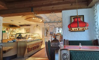 A cozy restaurant with an inviting atmosphere. The decor is rustic, featuring a striking red lamp and a view of the counter. | © Kleinwalsertal Tourismus | N. Lughammer
