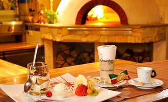 A delicious dessert on an elegant plate, including ice cream and fresh fruit. A kitchen oven is visible in the background. | © Ristorante Trentino | Michael Monschau