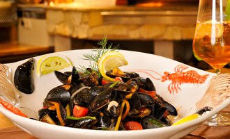 A delicious dish with mussels, vegetables, and lemon slices. In the background, there is a glass with a refreshing drink. | © Ristorante Trentino | Michael Monschau