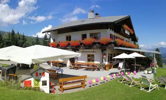 A charming alpine house with blooming balcony boxes and an inviting terrace. The surroundings are green, and the view of the mountains is breathtaking. | © Cafe Walserblick | Marcus Dornach