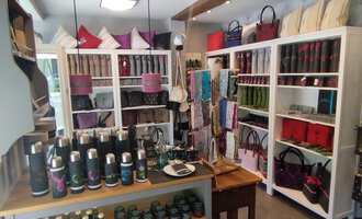 A stylish store with shelves displaying various bags and accessories. On a table in the foreground are various water bottles and products arranged. | © Chrömle Schönes aus Filz | N. Lughammer