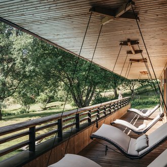 Eine entspannende Veranda mit modernen Liegen und Blick auf einen grünen Garten. Die Holzdecke und die natürliche Umgebung schaffen eine ruhige Atmosphäre. | © Naturhotel Chesa Valisa | Heldentheater