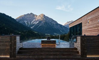 Ein Infinity-Pool mit Blick auf majestätische Berge. Die Holzveranda schafft eine gemütliche Atmosphäre in der Natur. | © Travel Charme Ifen Hotel
